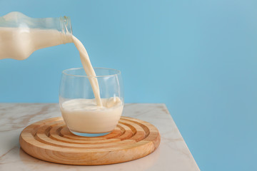 Pouring of milk into glass on table against color background