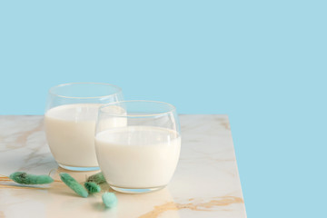 Glasses of milk on table against color background