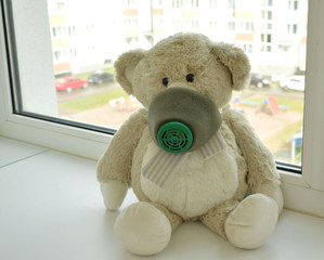 Teddy bear in a respirator sitting on the windowsill, coronavirus, quarantine, self-isolation, protection, bandage