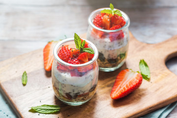 Yogurt granola parfait with strawberries and chia seeds. Healthy single portion breakfast served in glass cups on wooden board with green napkin. Natural wooden table background