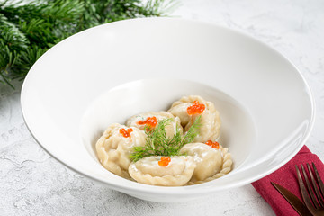 Dumplings in a white deep plate decorated with red caviar