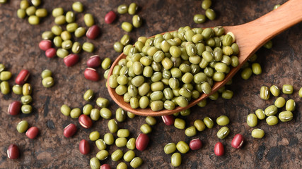 close up of green bean in wooden spoon with red beans on wooden background