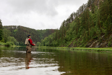 Fototapeta na wymiar Fly fishing. Elderly Fisherman alone stand in river water. Hobby sport activity