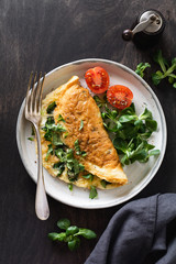 Stuffed omelette with tomatoes, red bell pepper, cream cheese and corn or lamb's lettuce on dark wooden background with copy space. Healthy diet food for breakfast. Top view, flat lay.