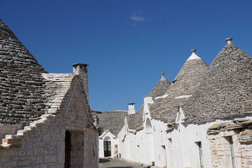 Fototapeta na wymiar Small street detail of white round houses with specific architecture and stone roof from unesco world heritage Trulli of Alberobello in Italy