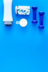Creatine capsules, protein near shaker and dumbbells - sports supplements - flat lay on blue background top view copy space