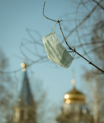 Medical mask hanging on a branch against the background of the Orthodox Church