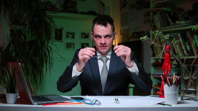 A cunning man after a party begins to do office work. Shows a gesture of silence. Deviant behavior. Home office during coronavirus infection COVID-19.