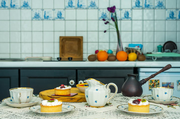 Cups, saucers, cakes on the table with a tablecloth.