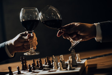 Close up of hands of men playing chess and drinking wine.	