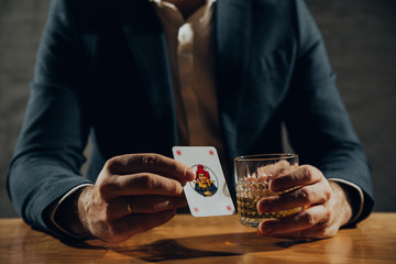 Close up of hands playing card and drinking whisky.	
