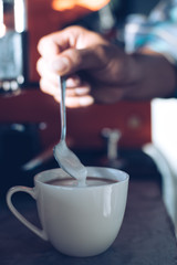 Barista pour the milk from a spoon into a coffee mug.