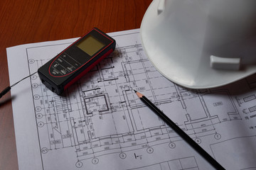Laser meter, white hardhat and drawings at engineer workplace