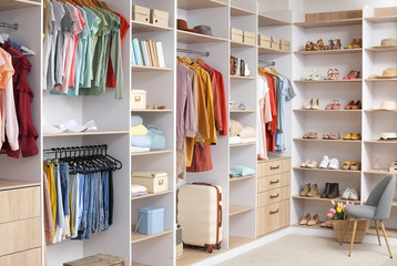 Big wardrobe with different clothes and accessories in dressing room