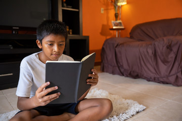 boy sitting reading in living room of his house with shorts and white shirt, in coronavirus quarantine in mexico