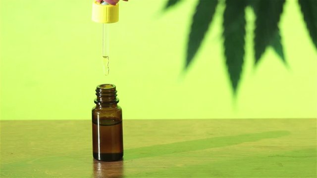 woman hand using dropper with cannabis cbd hemp oil dripping in to glass bottle 