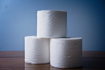 Three Rolls of Toilet Paper Stocked Up on Wooden Bathroom counter. Essential toiletries and basic hygiene necessity. Washroom products stock piled for pandemic. Coronavirus Covid 19. Soft TP 