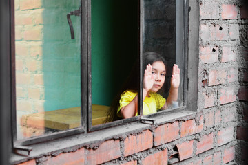 Serious little latin girl standing near window.