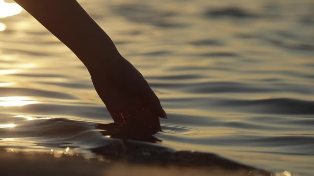 Silhouette of female hand put hand into a sea water