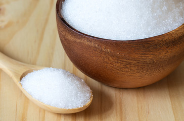 Bowl and spoon with white sand sugar on wooden background..