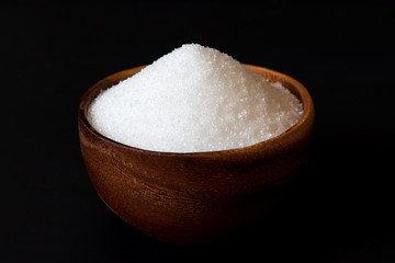 Fototapeta na wymiar White sand sugar in wooden bowl on black background..