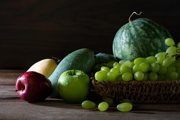 Fresh fruits and green grape in basketry basket on the table and dark wooden background which has dim light