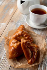 Traditional russian stuffed patties with golden crust, served on wooden table with a cup of tea