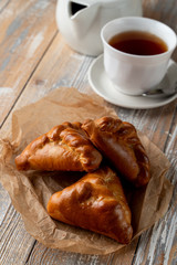 Traditional russian stuffed patties with golden crust, served on wooden table with a cup of tea