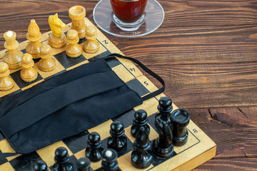 Handmade old chess on a wooden board. Occupation on vacation and quarantine. Nearby is a cup of...