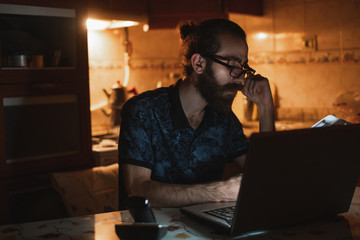 Fototapeta na wymiar Stressed young hipster long hair bearded man is checking invoice in the kitchen.