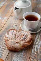 Traditional russian moscow sweet bun with powdered sugar on top, sugar pastry swirl on wooden background with a cup of tea