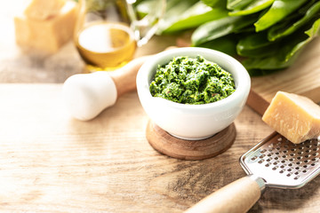 Wild leek pesto with olive oil and parmesan cheese in a white ceramic mortar on a wooden table. Useful properties of ramson.