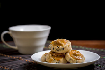Cashew nut and black seasame cookies on white dish and wooden table with blurry cup of coffee on black background. Coffee time concept.