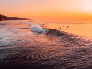 Aerial view of surfer and wave in ocean at warm sunset.