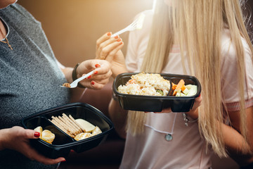 Two female colleagues eat from a food container.