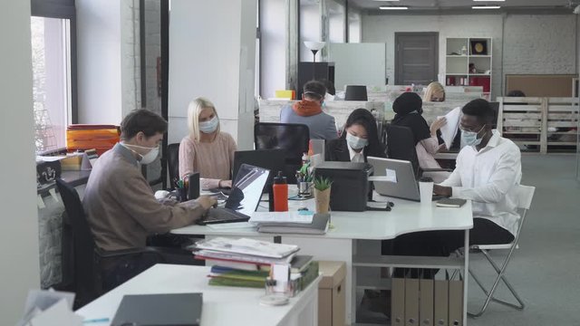 international office, working and communicate in an open space, office workers and managers in medical masks working at computers, protection from the virus, working during the pandemic.
