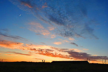 Fototapeta na wymiar Beautiful sunset with moon over farm silhouette, sunlight on horizon of golden pink sky with clouds