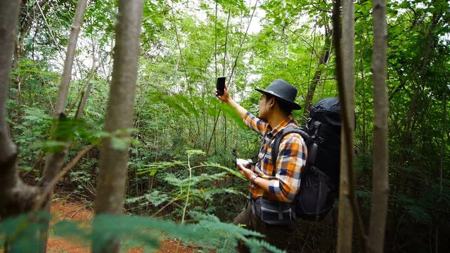 man traveler with backpack using smartphone to taking a selfie in the natural forest