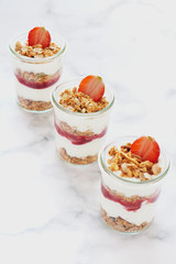 Small jars of granola with yogurt-strawberry jam and fresh strawberries.