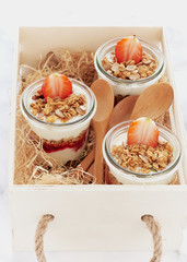 Small jars of granola with yogurt-strawberry jam and fresh strawberries served in a wooden tray.