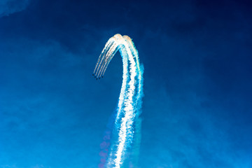 Group of five small planes crossing the blue sky and leaving the coloured smoke mark behind them. Airshow of small aircrafts making maneuvers in the sky