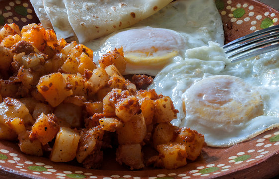 Over medium eggs with potatoes and chorizo or huevos estrellados con papas y chorizo, on a Mexican mud or clay plate as part of a Mexican breakfast. 