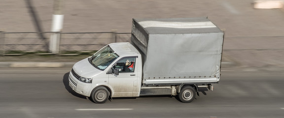 white van in motion on the city road shipping goods. Delivery van fast delivers in a city. Truck with an awning driving with motion blur effect