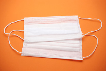 Two disposable medical masks on an isolated orange background.