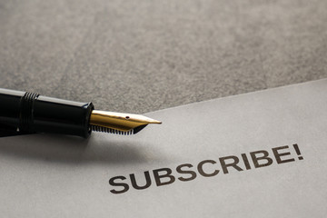 Symbolic pen and sheet of paper on a desk showing the text SUBSCRIBE!