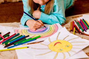 Cute little girl draws at home. A child draws a sun and a rainbow