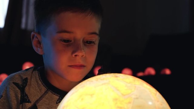 Portrait of little boy exploring a large globe in a dark room and dreaming about new travel