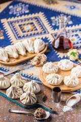 Fototapeta na wymiar Traditional Caucasian cuisine. Raw dumpling or khinkali with meat, mushroom and potato laid out on a cutting board on a wooden table with a towel, rolling pin, vegetables and spices.