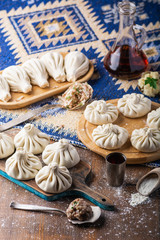 Traditional Caucasian cuisine. Raw dumpling or khinkali with meat, mushroom and potato laid out on a cutting board on a wooden table with a towel, rolling pin, vegetables and spices.