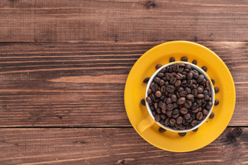 yellow cup filled with coffee beans on brown wooden boards. top view